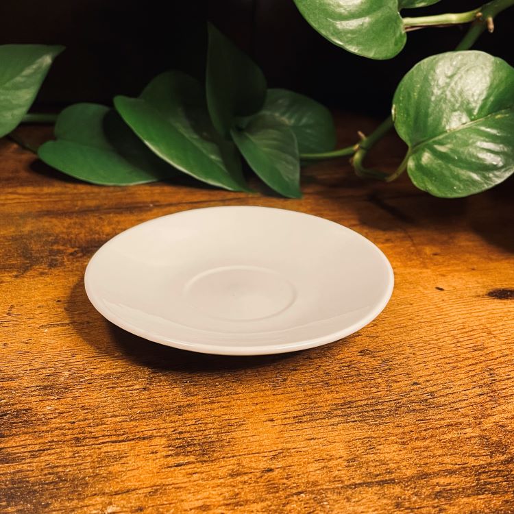 White ceramic plate on a wooden surface with green leaves in the background