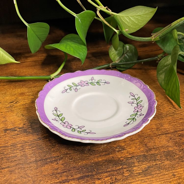 Decorative saucer with purple rim and floral patterns on a wooden surface with green leaves in the background