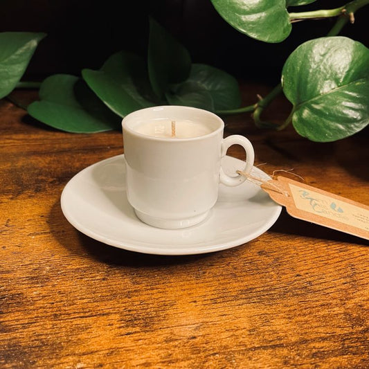 White cup and saucer with a candle on a wooden surface with green leaves in the background