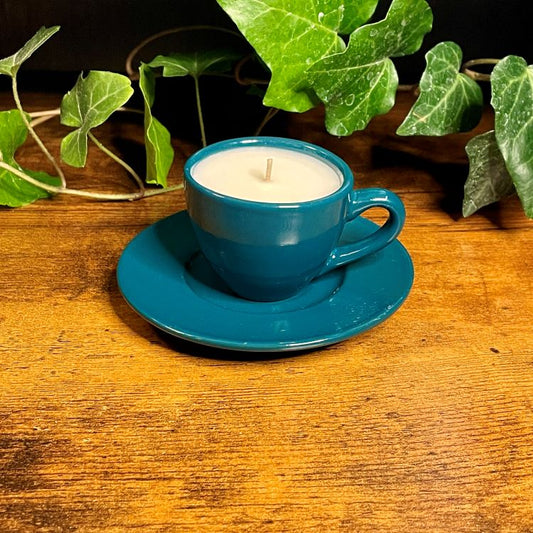 Turquoise cup and saucer with a candle on a wooden surface with green leaves in the background