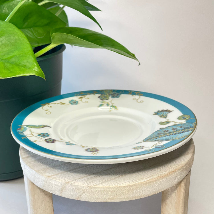 Decorative ceramic saucer with floral patterns on a small wooden stool next to a potted plant.