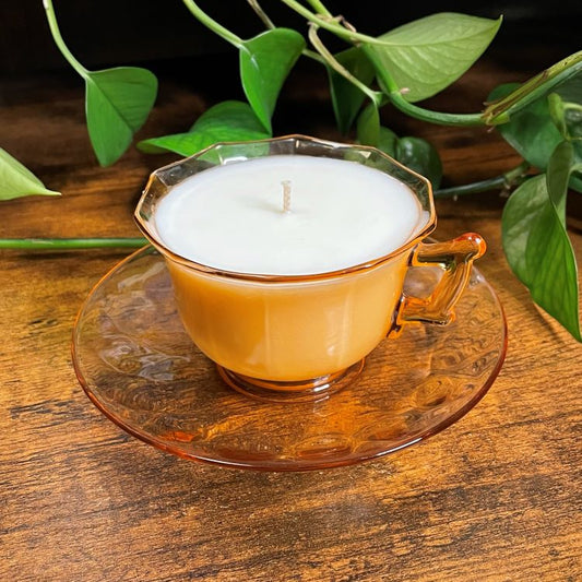 Candle in a glass teacup on a wooden surface with green leaves in the background