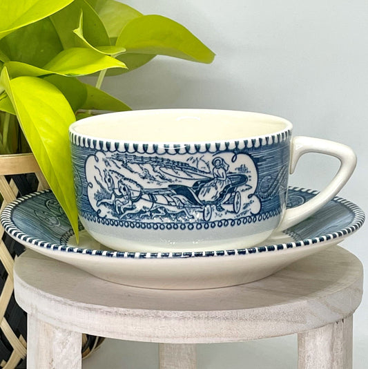 Teacup and saucer with blue floral design on a wooden table with a plant in the background