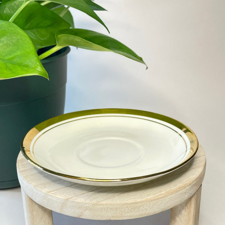 White plate with gold rim on a wooden stool next to a potted plant