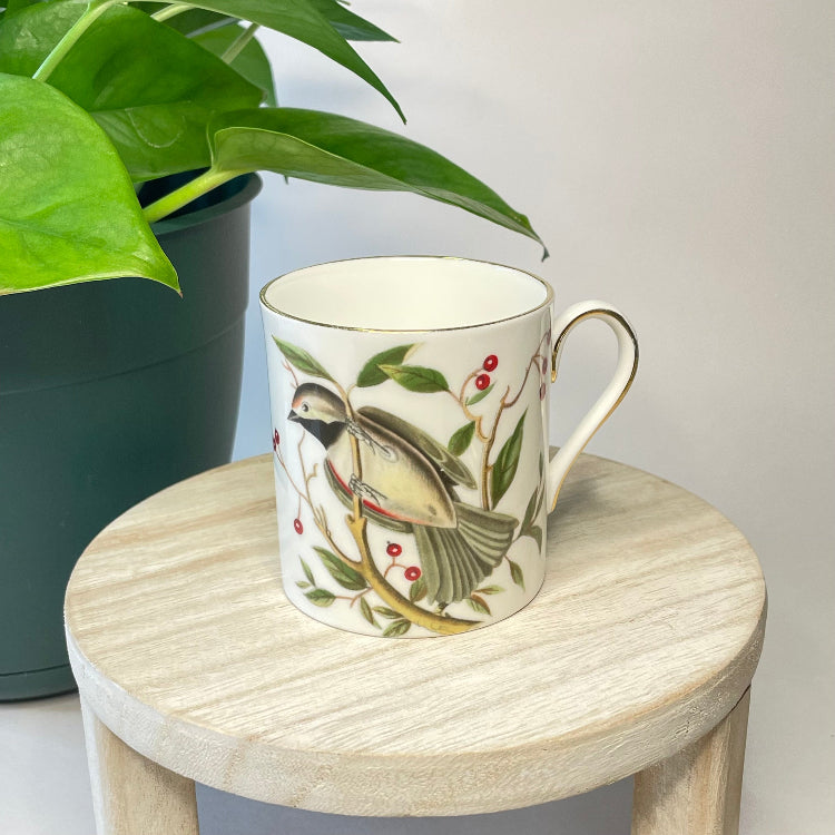 Ceramic mug with bird design on a wooden stool next to a plant