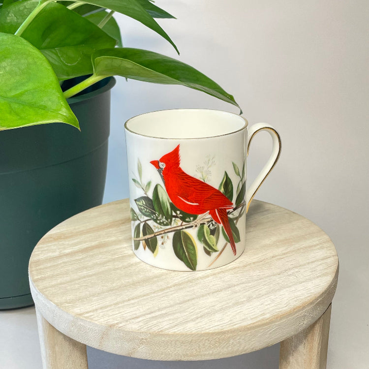 Mug with a red bird design on a wooden stool next to a potted plant
