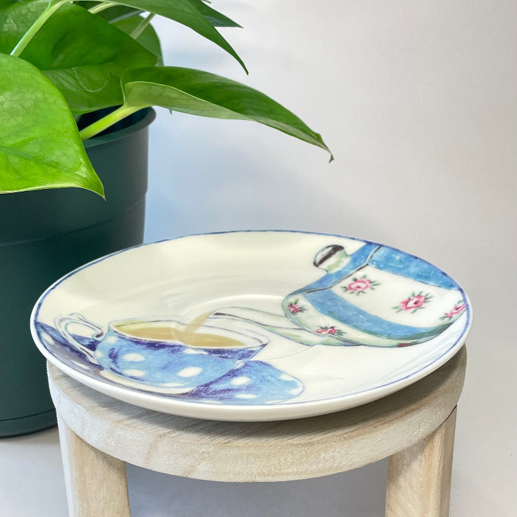 Decorative saucer with tea cup design on a small stool next to a potted plant.