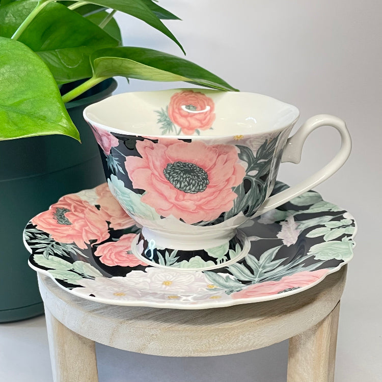 Floral teacup and saucer set on a small wooden stool with a plant in the background.