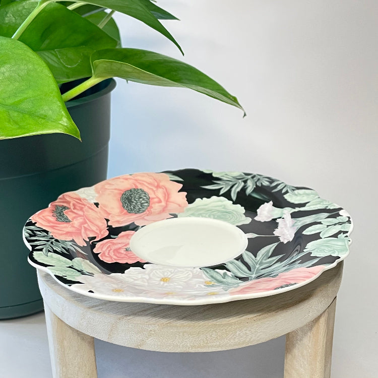Decorative saucer with floral design on a small stool next to a potted plant.