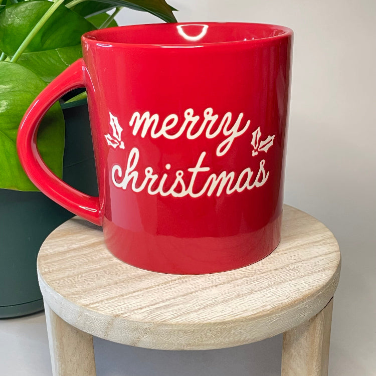 Red mug with 'merry christmas' text on a wooden stool