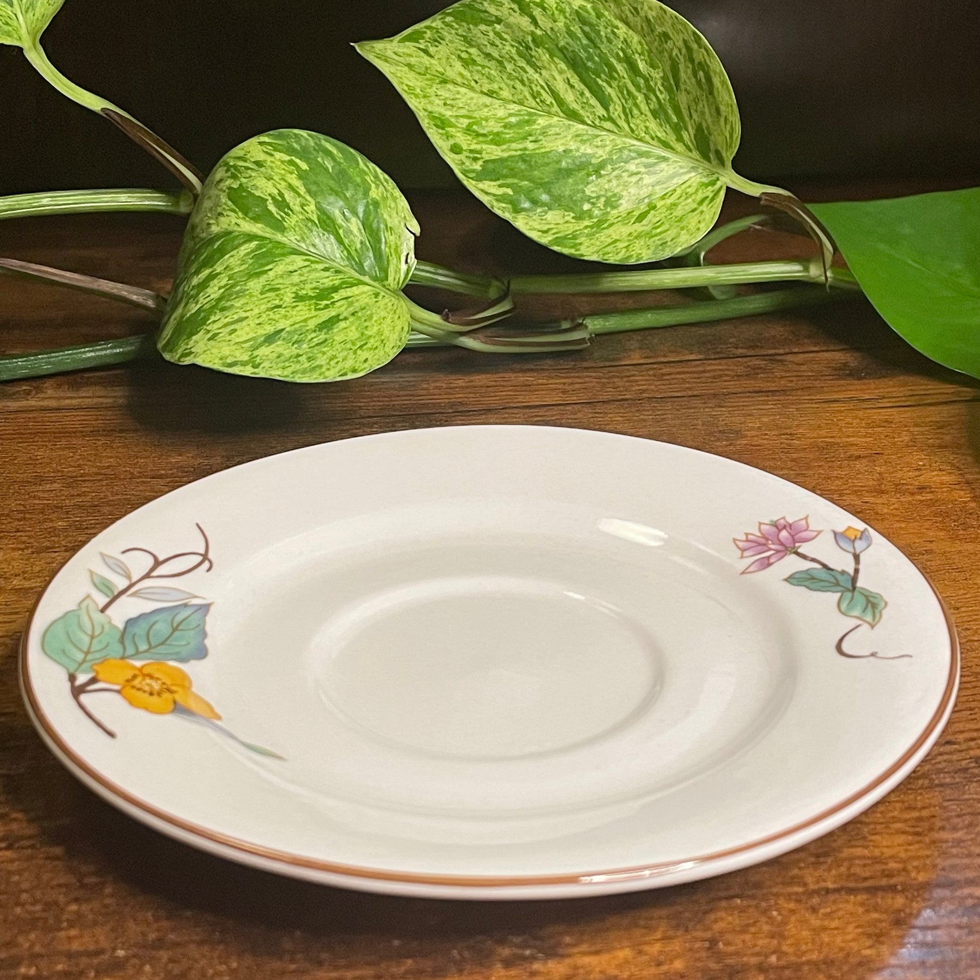 White decorative saucer with floral designs on a wooden surface with green leaves.