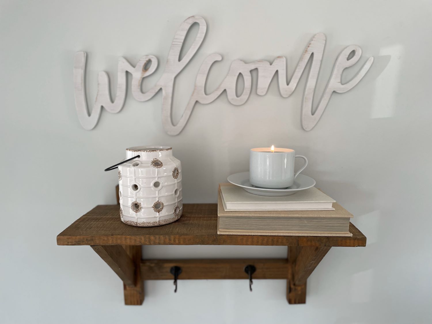 Wooden shelf with 'welcome' sign, candle, and books against a light gray wall.